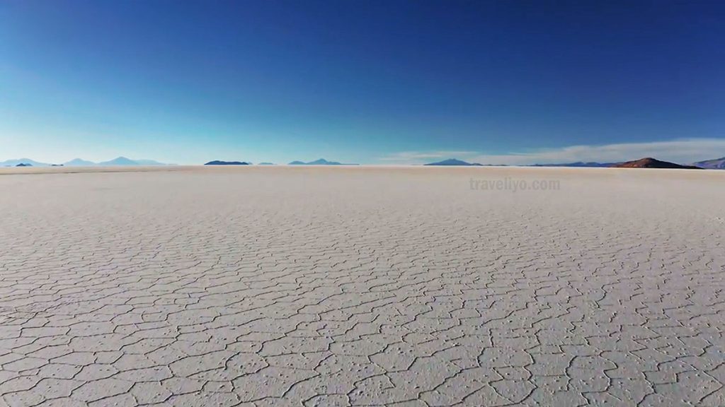 A vast, cracked hexagonal pattern on the dry surface of the Uyuni Salt Flats under a clear blue sky