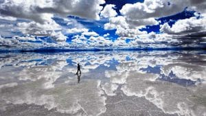 A stunning wide-angle shot of a person standing on the Uyuni Salt Flats in Bolivia, perfectly reflected in the shallow water, creating a surreal mirror effect
