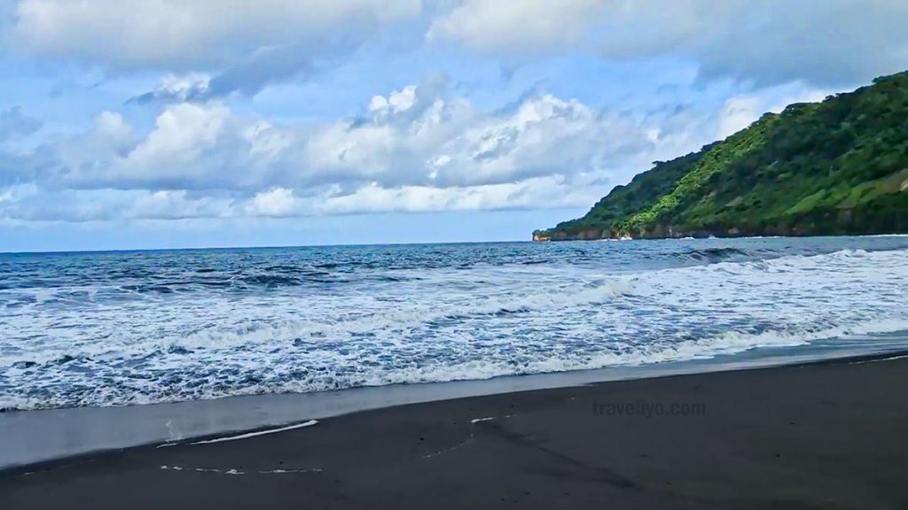 Black sand beach on Tanna Island surrounded by green hills and ocean waves