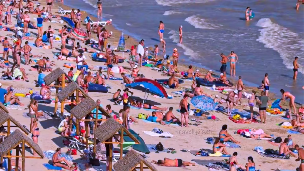 A bustling, crowded scene of locals and tourists enjoying the sunny Al-Ghandour public beach in Aqaba.