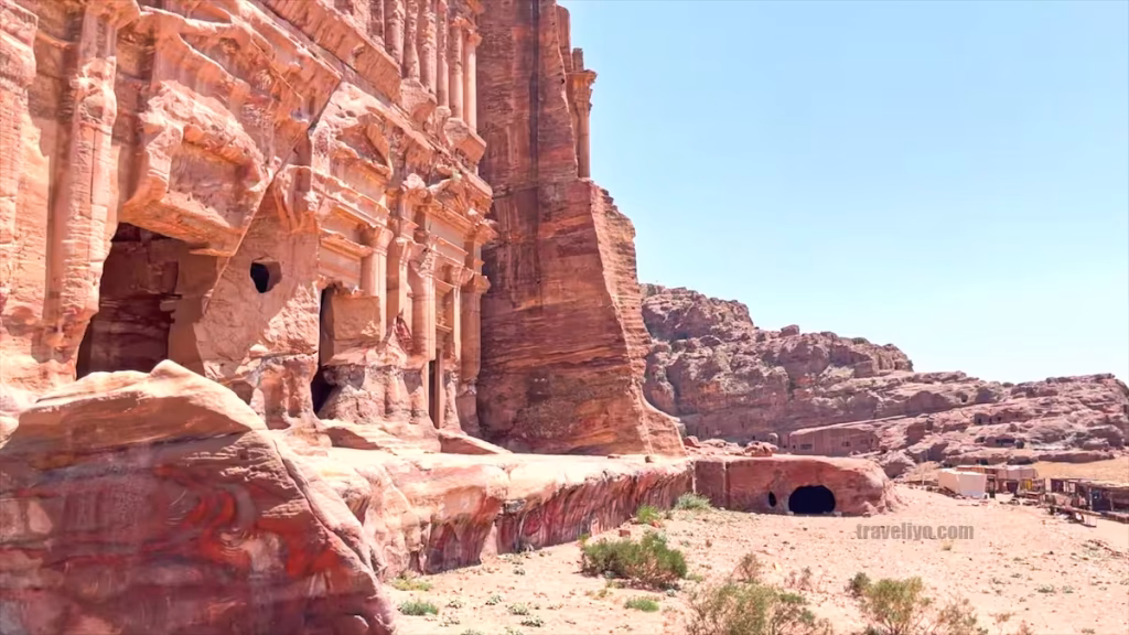 Large rock-cut caves and tomb openings carved into the lower pink sandstone mountains of Petra.