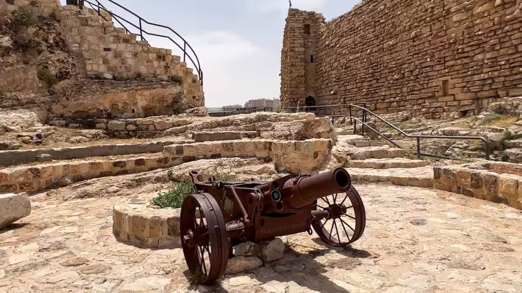 An ancient iron cannon on a wooden carriage sitting in an open stone courtyard at the al karak castle in jordan.