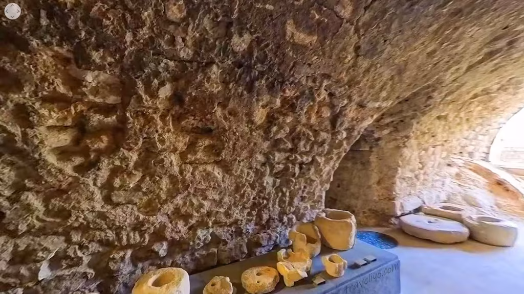 Old pottery vessels and round stones displayed inside a rocky chamber at Shobak Castle in Jordan.