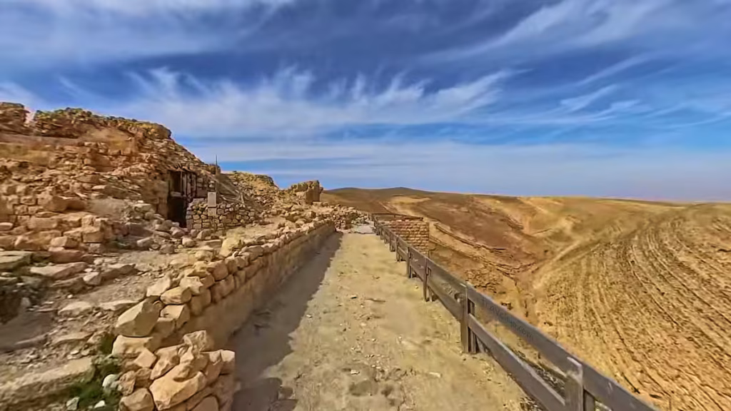 A straight stone pathway with a wooden safety railing looking out over the mountains at Shobak Castle in Jordan.