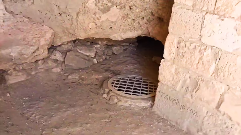 A rocky underground cave area with a metal grate covering a deep shaft at Shobak Castle in Jordan.