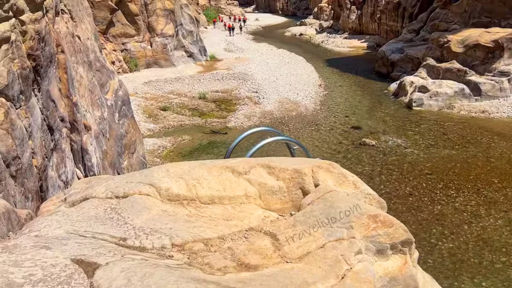 Looking down from the entrance bridge at the shallow riverbed winding into Wadi Mujib.