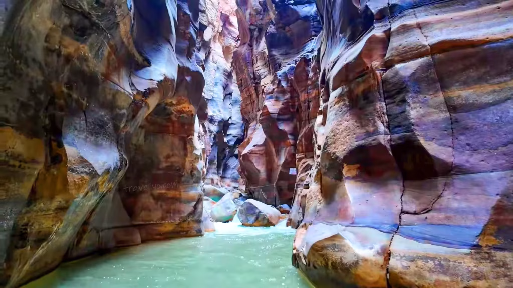 A breathtaking view of the colorful pink and purple sandstone gorge of Wadi Mujib Jordan with flowing turquoise water.