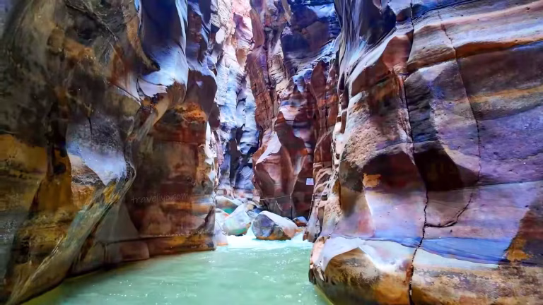 A breathtaking view of the colorful pink and purple sandstone gorge of Wadi Mujib Jordan with flowing turquoise water.