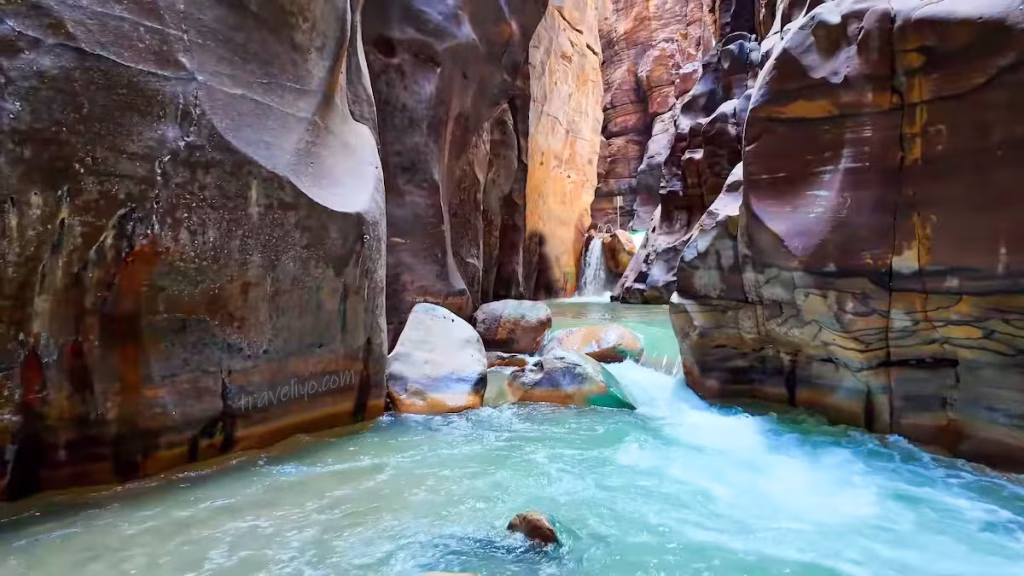 Rushing white water rapids and a small cascade between narrow canyon rocks on the Wadi Mujib Siq Trail.