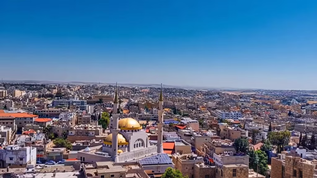 A sweeping panoramic view over the historic city of Madaba, Jordan, showing local mosques and residential homes.