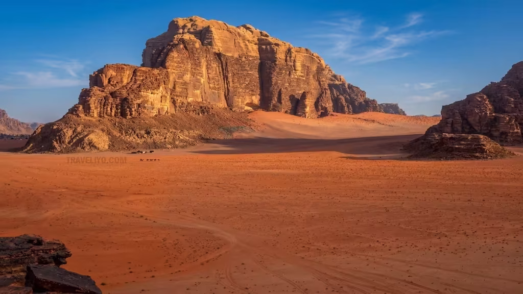 Massive red sandstone mountains rising from the desert floor in Wadi Rum.